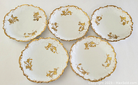 Top view of five Limoges porcelain plates, showing gold floral designs and scalloped gold edges.