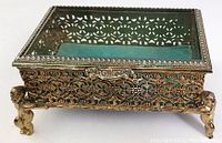 Front and side view of rectangular metal trinket box with ornate floral design and glass top