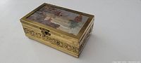 Angle view showing the top and side carved brass detailing with glass lid showing painted landscape.