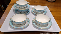 Five Wedgwood two-handle cups and matching saucers on a white tray showing the top view of the cups and detailed matching pattern.