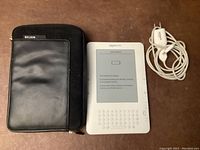 Amazon Kindle front with low battery screen, Belkin case beside it, charging cable and adapter above.