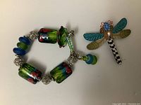 Photo showing the full artisan bracelet with colorful glass beads and silver metal accents next to the dragonfly brooch