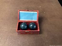 Pair of Baoding balls in red decorative box with blue paper insert inside the lid, placed on a brown surface.