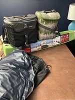 Two soft coolers (black and camouflage) placed on top of boxed beach shade tent on table.