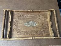 Top view of the carved wooden serving tray with floral border carving and central inlay design, showing handles.