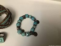 Close-up of bracelet made with large turquoise stone beads and silver-tone metal spacers and charm.