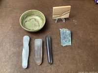 Photo showing stone bowl, three crystal wands, unpolished jade, and small sandstone piece on wooden stand.