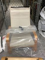 IKEA Poang chair wooden frame without cushions wrapped in plastic bag, beige fabric seating support attached to the frame