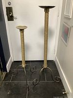 Two large metal candle holders with rope-wrapped stems and curled three-legged bases next to a door