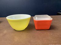 Small yellow mixing bowl and small orange square covered dish with clear lid, shown on table