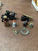 Antique Merck poison bottle with cork labeled 'Sparting Sulphate' and various small figurines including cast metal animals, miniature cannons, porcelain figure, metal frog, and decorative pins on a wooden surface.