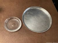 Photo of metal tray and crystal ashtray set on brown surface