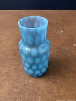 Blue glass vase with raised coin dot pattern against brown surface.