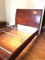 Wide view showing the full sleigh bed frame from the foot side, highlighting the side rails and metal support bars.