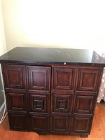 Full view of the dark wood cabinet with paneled doors and black stone top showing scratches and minor damage.