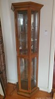 Front-right angled view of tall wooden curio cabinet with glass panels and mirror back.