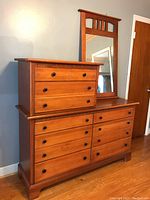 Side-angle photo of wooden dresser and matching mirror, showing drawer layout and wood finish.