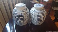 Pair of matching blue and white ceramic ginger jars with lids placed on a dark wooden table, showing the overall design and size.