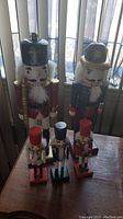 Photo showing five wooden nutcracker figurines on a wooden surface in front of a window, two large and three small.