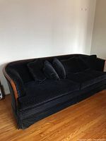 Front view of the black upholstered sofa with wood accents and matching cushions on hardwood floor against white wall.