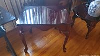 Wooden side table with curved decorative edges and carved legs shown from an angled side view on hardwood floor.