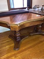 Side close-up of table leg, showing carved wooden pedestal leg design and underside of tabletop corners.