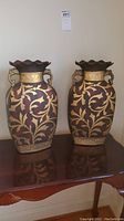 Front view of both matching decorative metal vases showing floral and vine pattern and scalloped rims with chips
