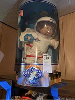 Full view of the doll in original packaging showing the doll's face, astronaut suit, and helmet.