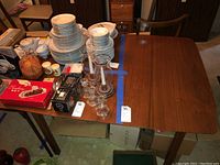 Dining table with items on top and visible tag, showing wood grain surface and removable legs.
