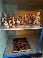 Full view of the 14 Goebel Hummel porcelain figurines displayed on a shelf with the Hummel book underneath