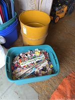 Yellow metal barrel next to blue storage tote, both containing matchbooks and paper collectors' items.
