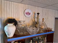 Wide view of lot showing various decorative vases, bowls, and decanters on a shelf including ceramic, glass, and metal materials in different shapes and sizes.