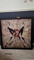 Full view of the square abstract canvas art with two black stylized female figures and textured beige background, framed in a black wooden frame with visible wear.
