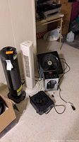 Five items on floor in basement setting with one plugged in device, including the Ionic Pro Air Purifier, multiple fans and a fan heater.