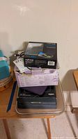 Stack of boxed electronics and cases including MyCharge wireless earbuds box, TCL tablet case, purple Kindle Fire HD case, and Samsung Digimax camera box.