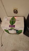 Closed original box of Bemis WaterWick humidifier model 7260 placed on floor near electrical outlet.