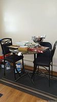 Full view of round metal bistro table with faux stone top and three chairs around it, table surface has various household items on it.