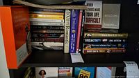 Shelf with multiple books of various genres stacked vertically and horizontally