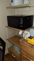 Photo of rolling kitchen cart showing three shelves and two drawers with a brown faux wood finish. A microwave is on the middle shelf.