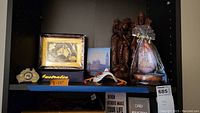 Shelf displaying seven foreign decor items including clocks, book, wood sculptures, carving and mask