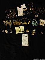 Photo showing 14 pairs of assorted earrings and 6 rings arranged on a black surface.