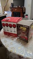 Boxes of four Mikasa ruby balloon goblets with clear stems and four Pier 1 Imports etched wine glasses on table.