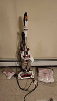 Full view of Shark upright vacuum cleaner with cord and attachments on the floor
