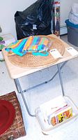 Wood and metal folding table with laminate wood grain top and gray metal folding legs. Table top shows minor wear.