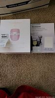 Boxed Dermalactives LED Light Therapy Mask and Brookstone Daylight Therapy Lamp together on carpeted floor.