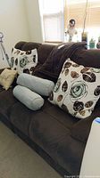 Couch holding four floral patterned square throw pillows, two blue bolster pillows, and dark brown plush throw blanket draped over the back