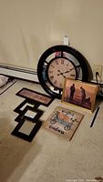 27-inch round wall clock with Roman numerals, gold-toned framed picture, decorative plaques, and rattan framed mirrors arranged on floor
