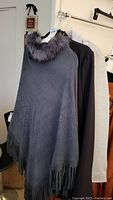 Gray poncho with faux fur collar hanging on rack with other jackets