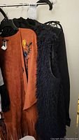 Side view of rust-colored floral poncho, black faux fur vest, and black jacket hanging on rack