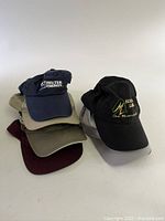 Seven caps stacked showing fronts with embroidered company logos and some plain colors